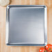 An American Metalcraft heavy weight aluminum pizza pan with tomatoes and cheese on a wood surface.
