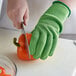 A person wearing green Mercer Culinary Millennia Cut-Resistant gloves cutting a bell pepper.