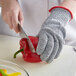 A person wearing a MercerMax Level Cut-Resistant glove cutting a red pepper.