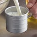 A person pouring milk into a Vollrath aluminum measuring cup.