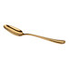 A gold-colored metal teaspoon with a smooth, reflective finish and a gently curved handle.