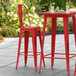 A Lancaster Table & Seating red metal barstool with black legs on an outdoor patio.