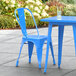 A blue Lancaster Table & Seating metal chair and table on an outdoor patio.