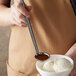 A person using a Vollrath stainless steel ladle to serve ice cream.