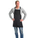 A man wearing a Mercer Culinary black canvas bib apron with black leather straps.