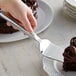 A hand using Vollrath stainless steel pastry server to slice a chocolate cake.