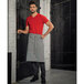 A man wearing a Mercer Culinary navy and white railroad stripe bistro apron with 3 pockets over a red shirt.