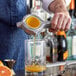 A person using a Westmark handheld juicer to pour orange juice into a glass.