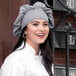 A woman wearing a Uncommon Chef Houndstooth twill chef hat with a smile.