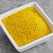 A white square bowl filled with yellow Regal Seasoned Salt powder on a table.