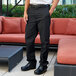 A man standing in a room wearing black Uncommon Chef straight leg chef pants.