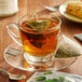A glass cup of Steep Cafe mint herbal tea with a tea bag on a saucer.