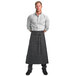A man wearing a long black Mercer Culinary Draper denim bistro apron with 2 pockets.