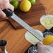 A person using a Microplane zester to zest a lemon over a glass of liquid.