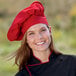 A woman wearing a red Uncommon Chef poplin chef hat with a white background.