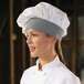A woman wearing a white houndstooth twill chef hat with a smile.
