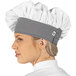 A woman wearing a white twill chef hat with a black houndstooth pattern.