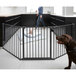 A person walking in a room with a baby and a dog behind a black BabyDan safety gate.