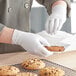 A person wearing Noble Products white nitrile gloves holds a cookie.