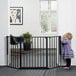 A little girl standing by a black L.A. Baby safety gate.