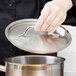 A hand holding a Vollrath Optio pan lid over a silver pot.