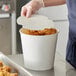 A person putting a paper lid on a Choice white food bucket of fried chicken.