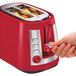 A hand pressing the button on a red Hamilton Beach toaster.