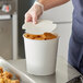 A person in gloves putting fried chicken in a white Choice food bucket.