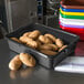 A black Carlisle bus tub on a school kitchen counter filled with potatoes.