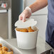 A person in gloves putting chicken in a white Choice food bucket.