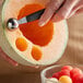 A hand using a Mercer Culinary melon baller to scoop a melon.