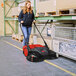 A woman pushing a Bissell Commercial battery powered floor sweeper.