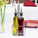 A Tablecraft Gemelli chrome rack holding a glass olive oil cruet and a glass vinegar cruet on a table.