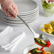 A hand using a Tablecraft Dalton slotted serving spoon to serve vegetables.