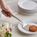 A hand holding a Tablecraft Dalton stainless steel solid turner over a plate of food with a piece of food on it.