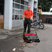 A man using a Bissell Commercial outdoor power sweeper to clean the sidewalk.