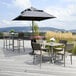 A Grosfillex Java taupe barstool with a wicker back on an outdoor patio with a table and chairs and an umbrella.