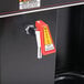 A black Bunn commercial automatic coffee brewer with a red and yellow warning label and red hot water faucet.