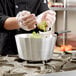 A person in gloves cooking green peppers and celery in a Vollrath Wear-Ever sauce pan.