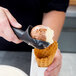 A person using a Zeroll ice cream scoop to add ice cream to a waffle cone.