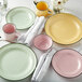 A table set with Luzerne pink plates with black borders, yellow plates, and green-rimmed plates.