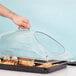 A hand using a Cambro clear glass dome cover to protect a tray of food on a counter.