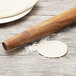 A Fox Run acacia wood French rolling pin next to a ball of dough on a table.