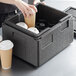 A woman putting a coffee cup into a Cambro Cam GoBox food pan carrier with cup holders.