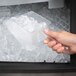 A hand using a Carlisle clear polycarbonate utility scoop to get ice from a clear plastic container.