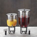 An American Metalcraft wrought iron base with two glass beverage dispensers filled with orange juice and water on a counter.