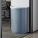 A gray Lavex half round trash can in a corporate office cafeteria.