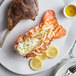 A plate with a Boston Lobster Company 24-28 oz. lobster tail, steak, and lemon slices.