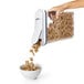 A hand pouring cereal into an OXO Good Grips rectangular food storage container with a white lid.