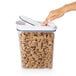 A hand opening an OXO Good Grips plastic food storage container with cereal inside.